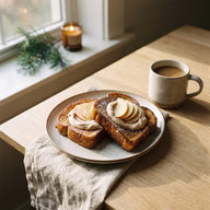 Zwei Scheiben goldbrauner French Toast mit Zimtschnecken Creme und Apfelspalten, daneben eine Tasse Kaffee