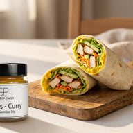 Zwei halbierte Wraps mit gebratenem Hähnchen, Salat, Gurke und gelblichem Aufstrich, daneben ein Glas Ananas Curry