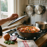 Ein Schmortopf mit Hähnchenkeulen in dicker Tomatensauce mit Paprika, Zwiebeln und Oliven