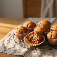 Goldbraune Muffins mit roten Johannisbeeren auf einem Kuchengitter, einer aufgebrochen