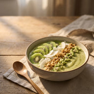 Eine Schale mit dicker, hellgrüner Smoothie-Masse, darauf Kiwischeiben, Kokosraspeln, Granola und knusprige Kiwistücke