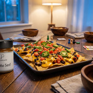 Ein Backblech mit Tortillachips unter cremiger Käsesauce, Bohnen, Tomatenwürfeln und Jalapeñoringen, daneben ein Glas Jalapeño Senf