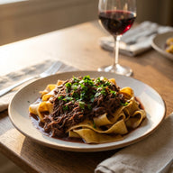 Breite Pappardelle mit dunklem Wildragout und frischer Petersilie auf einem Teller