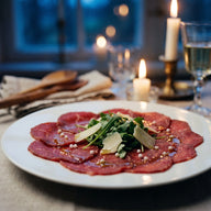 Hauchdünne Scheiben rohes Rinderfilet auf einem Teller mit Rucola, Parmesan und weißen Salzperlen