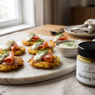 Kleine goldbraune Rösti mit Räucherlachs und einem Klecks heller Dill-Senf-Sauce auf einer Platte