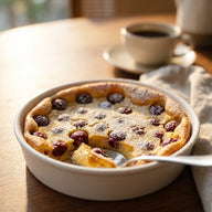 Ein goldgelber Clafoutis in einer runden Form mit dunkelroten Sauerkirschen, mit Puderzucker bestäubt