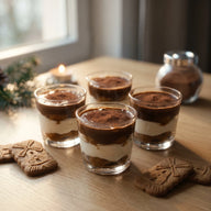 Vier Gläser Tiramisu mit Schichten aus Spekulatius, dunkler Kaffee Creme und Mascarpone, mit Kakao bestäubt