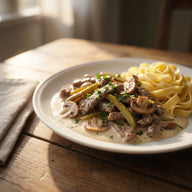 Ein Teller mit Rinderstreifen und Champignons in heller, cremiger Sauce, dazu Bandnudeln und Petersilie