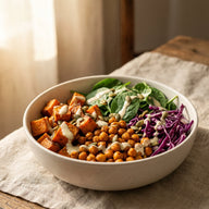 Eine Schale mit gerösteten Süßkartoffelwürfeln, knusprigen Kichererbsen, Spinat, Rotkohl und hellem Dressing