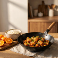Knusprige Hähnchenstücke in glänzender orangefarbener Sauce mit Frühlingszwiebeln und Sesam im Wok, daneben Reis
