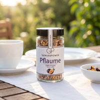 Kleines Glas gefriergetrocknete Pflaume von Genusspower auf einem Gartentisch, daneben Kaffeetasse und Schale
