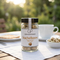 Kleines Glas gefriergetrocknete Stachelbeere von Genusspower auf einem Gartentisch, daneben Kaffeetasse und Schale
