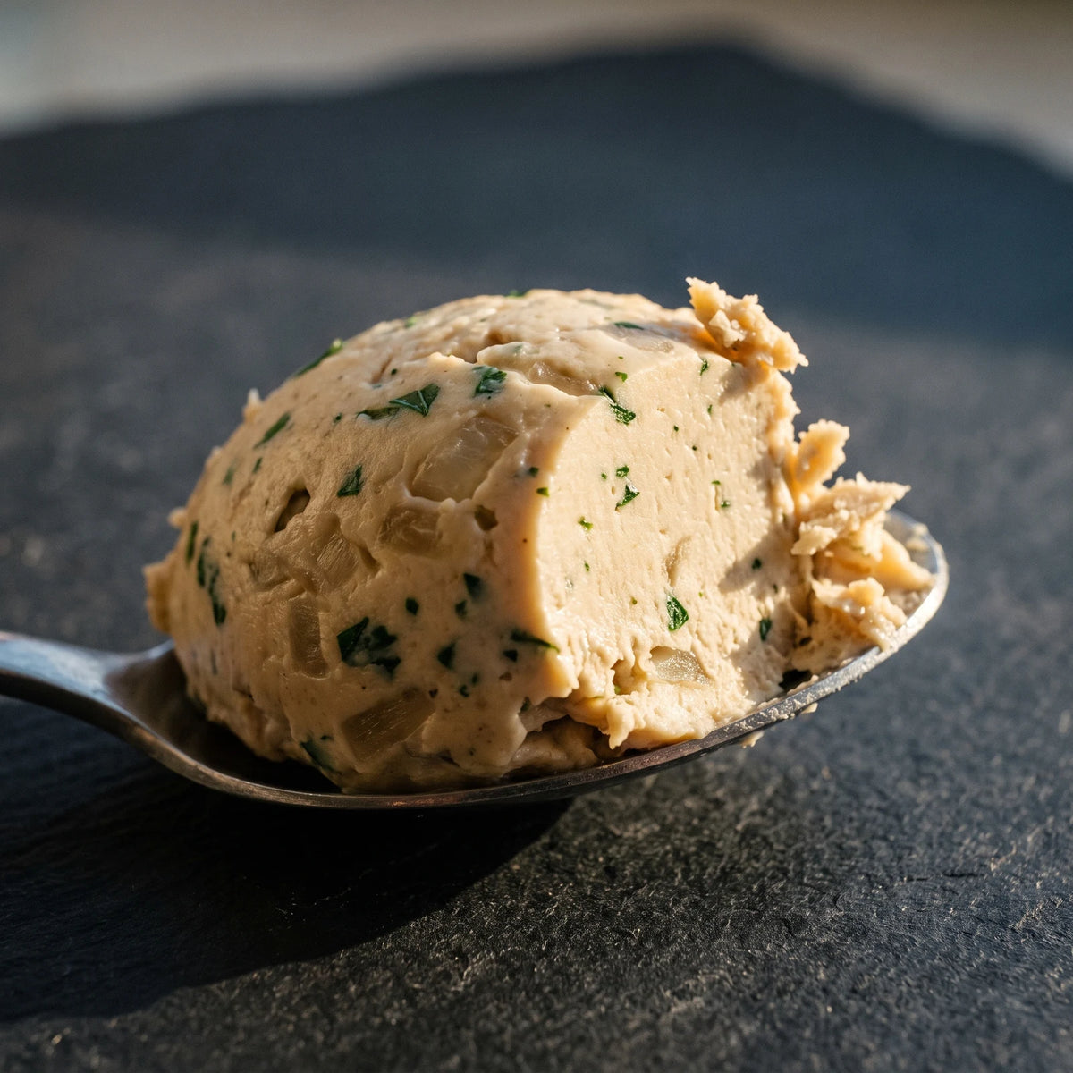 Makroaufnahme: ein Löffel hebt den cremigen Apfel-Zwiebel-Aufstrich, Petersilienflecken und Zwiebelstücke sichtbar