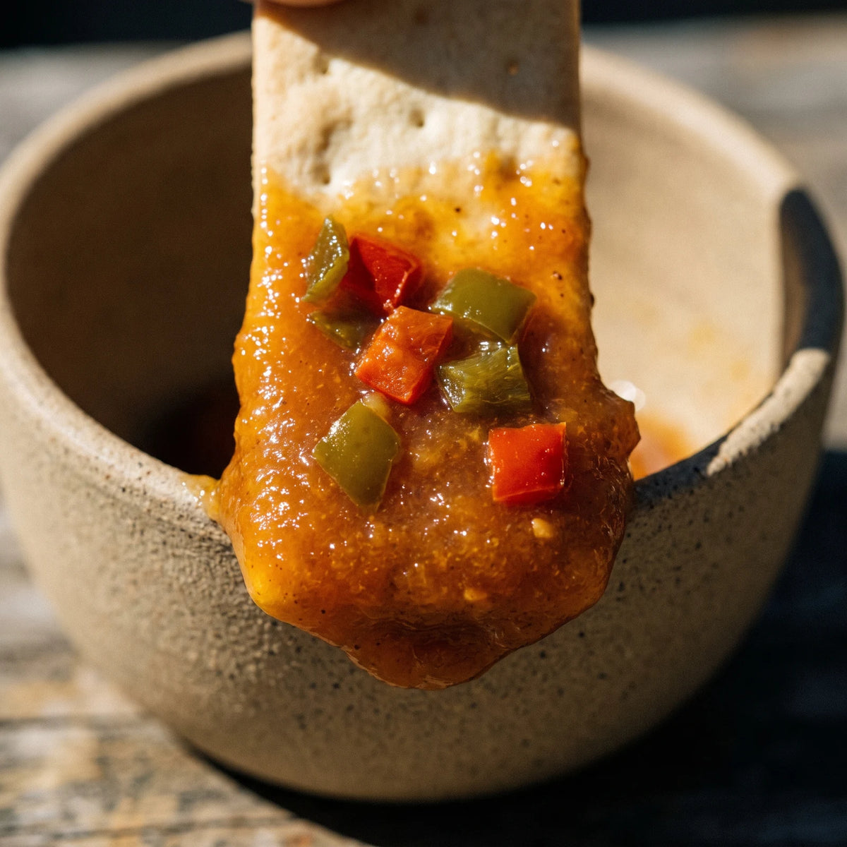 Makroaufnahme: ein Cracker steht im Chili-Mango-Aufstrich, gewürfelte rote und grüne Paprika im dicken Überzug sichtbar