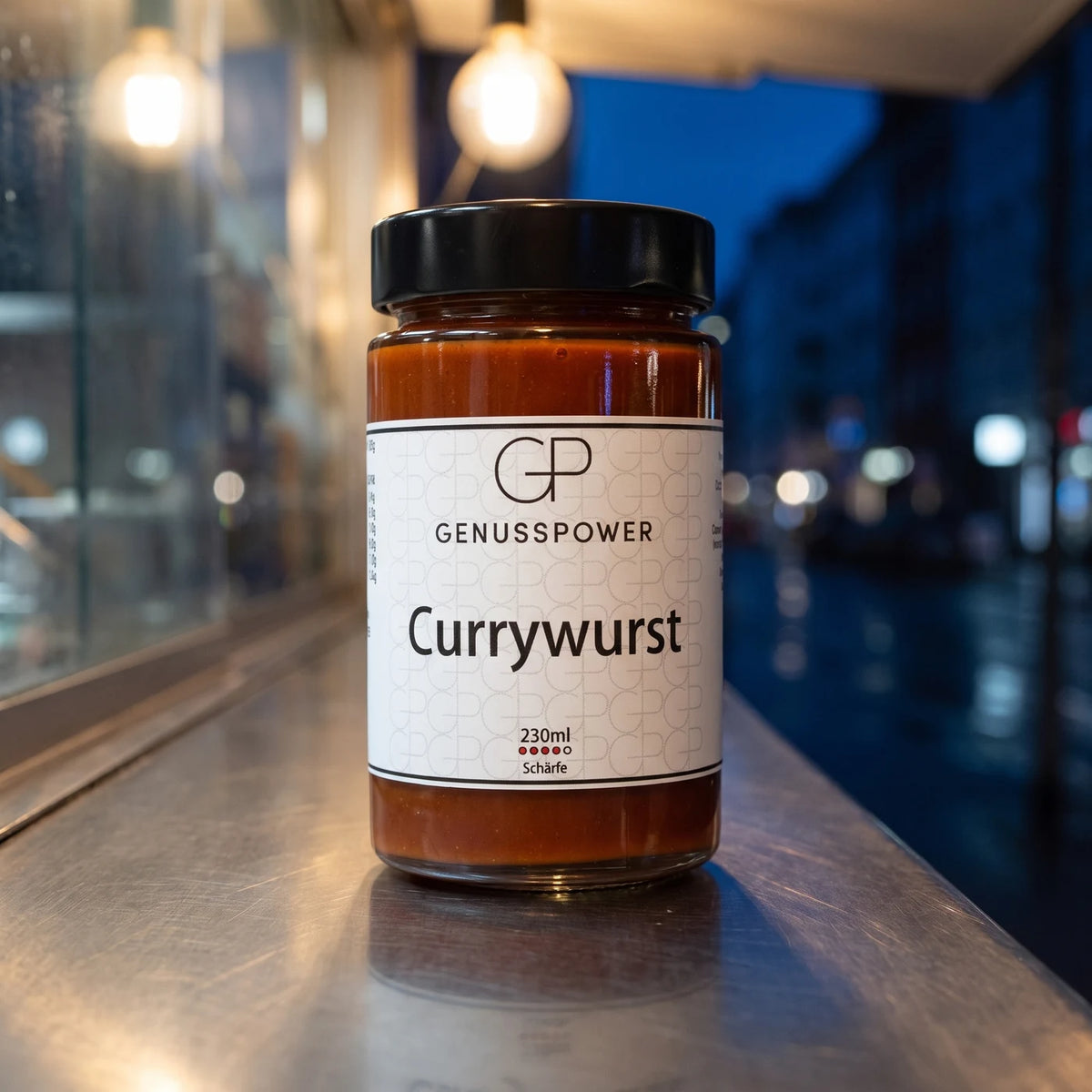 Glas Currywurst auf einer Edelstahltheke bei Nacht, dahinter die nasse Straße