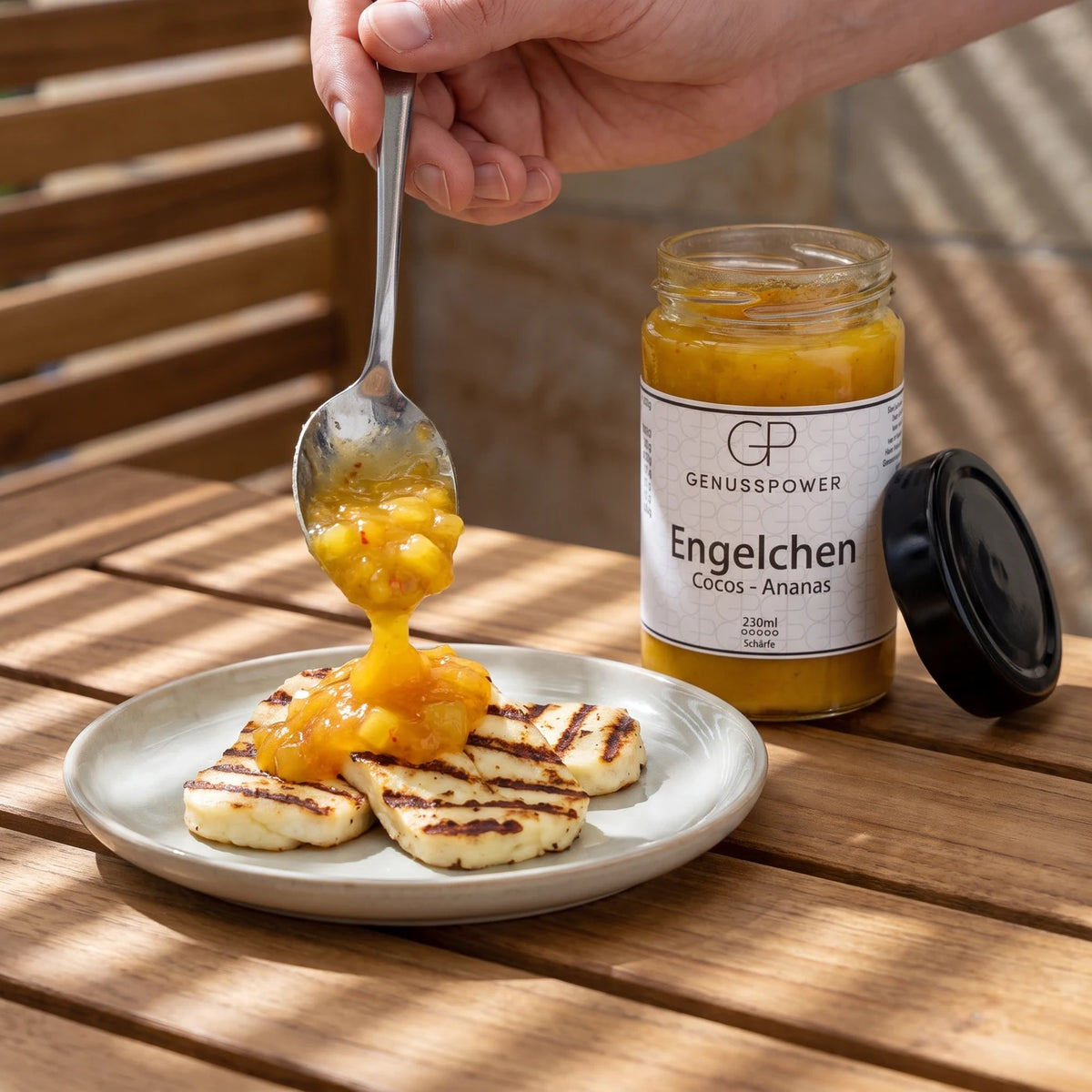 Ein Löffel gibt die goldgelbe Sauce über gegrillten Halloumi, daneben das offene Glas Engelchen