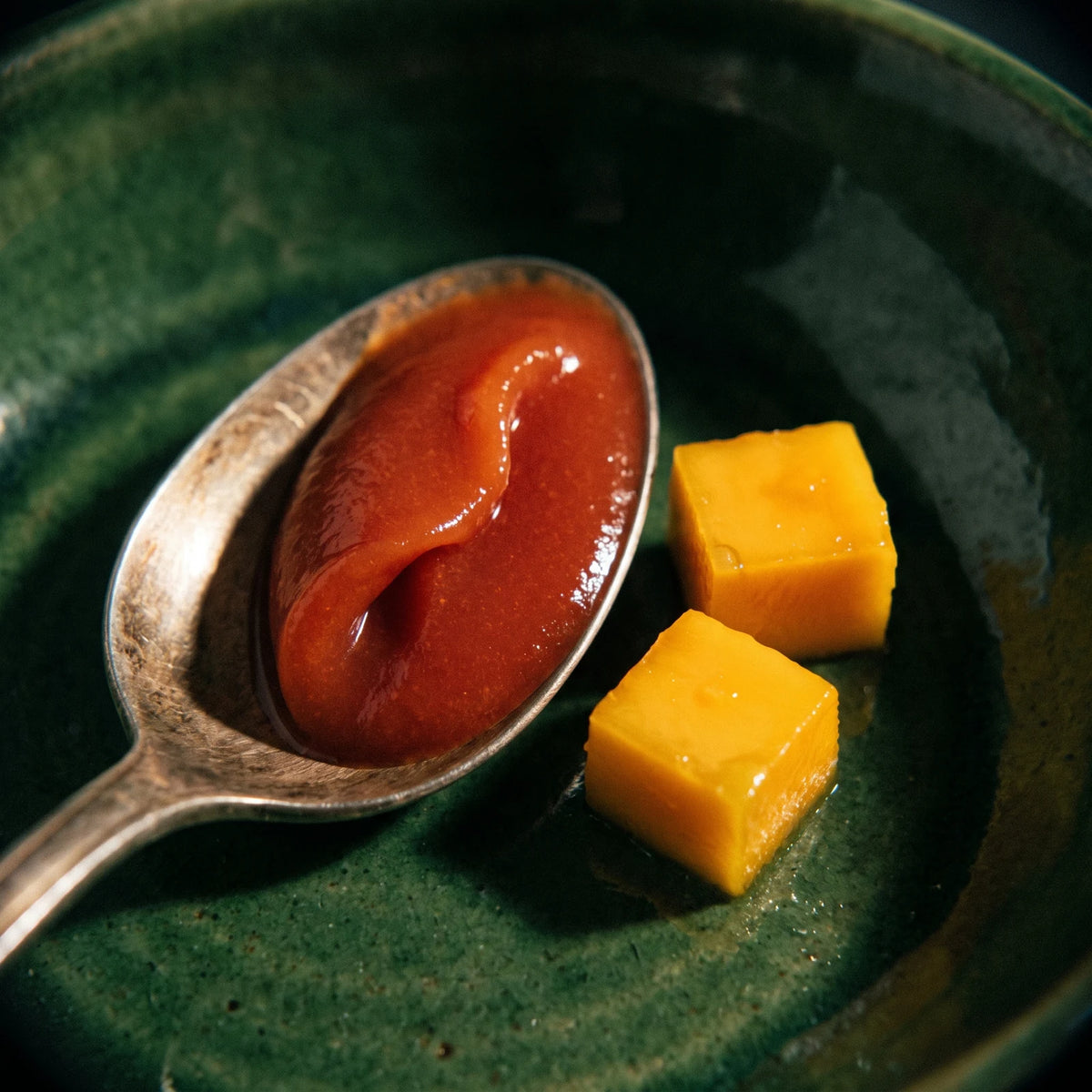 Makroaufnahme: ein Löffel mit glattem Feurige-Mango-Dip, daneben zwei Würfel weiches Mangofleisch