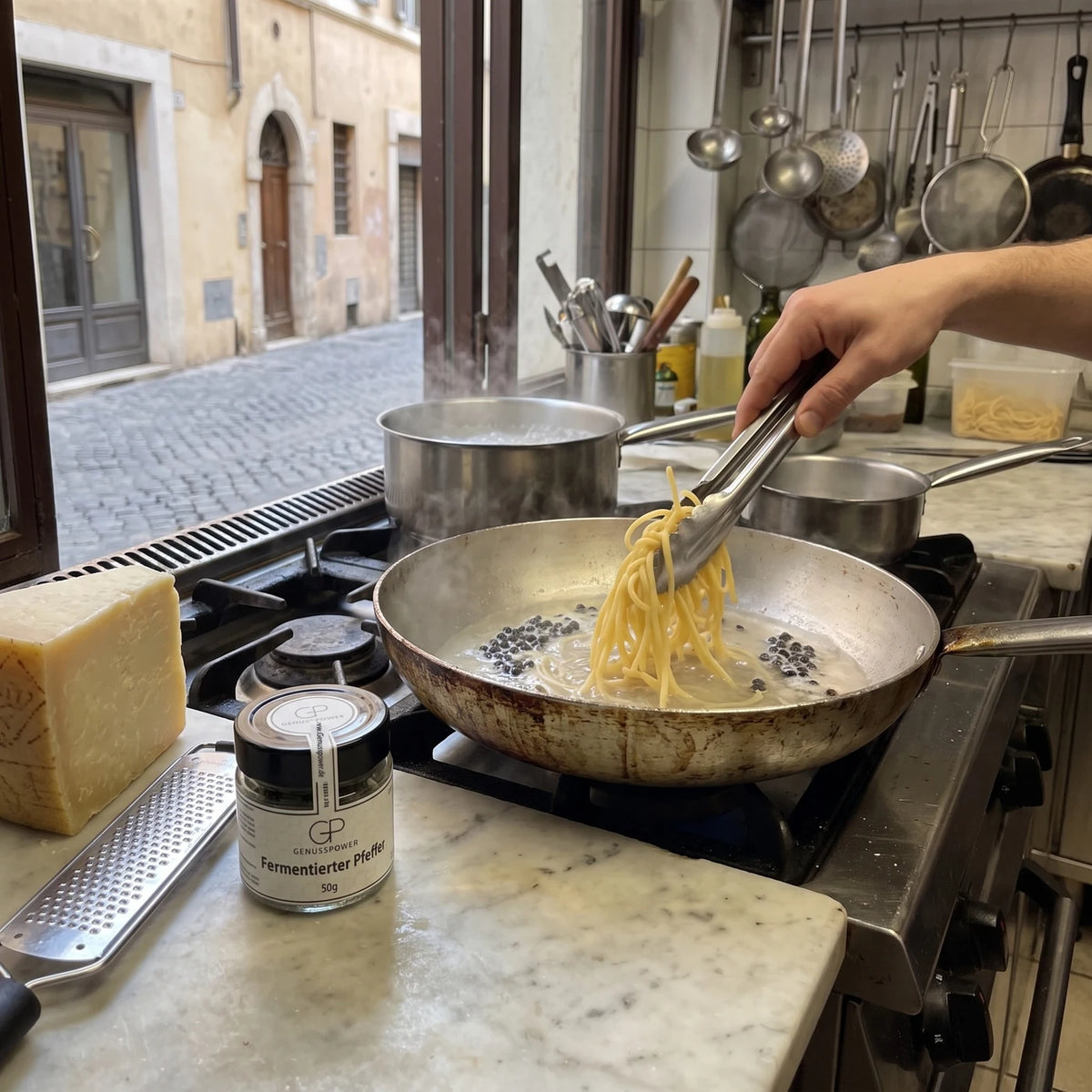 Koch gibt Pasta in die Pfanne mit Pastawasser und fermentiertem Pfeffer, daneben das Glas und Pecorino