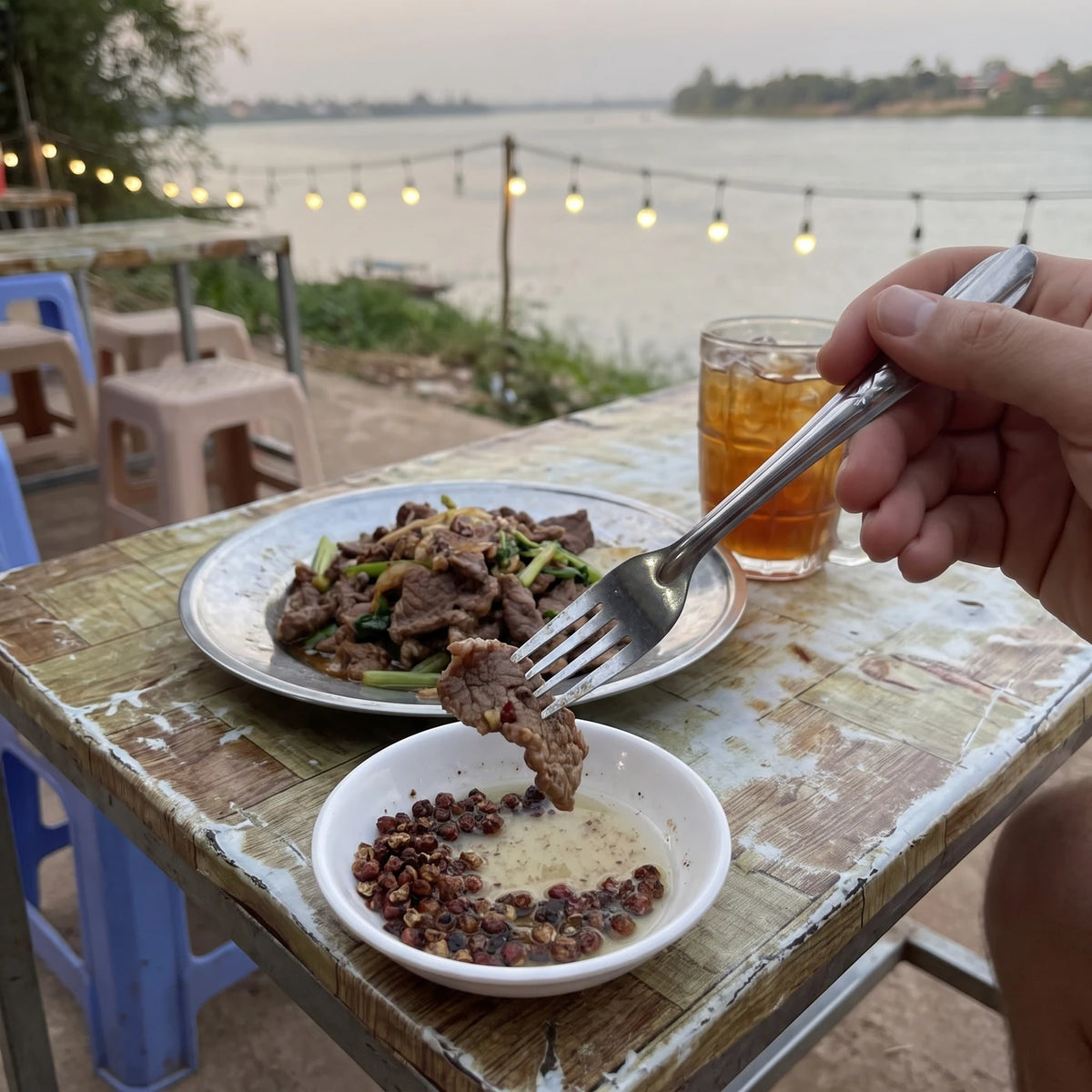 Gabel tunkt ein Stück Rindfleisch in einen Dip aus Limette und Kampot Pfeffer, Lokal am Fluss in Kampot