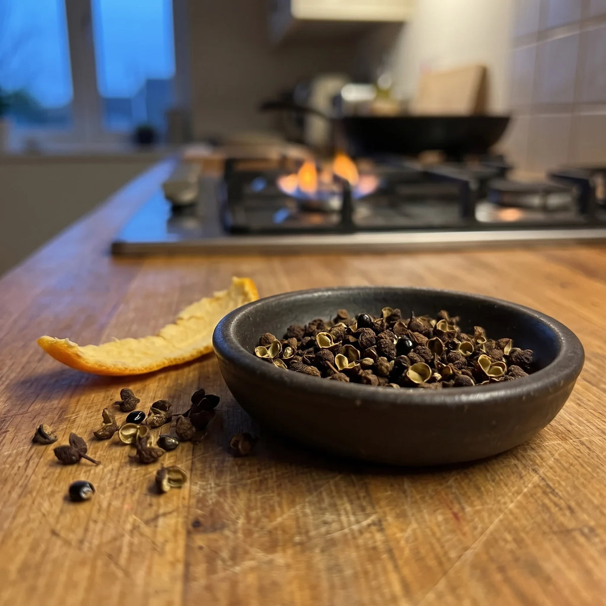 Dunkles Schälchen mit Mandarinen Pfeffer auf der Holzarbeitsplatte, daneben Mandarinenschale