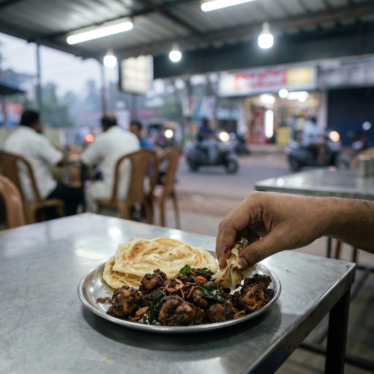 Pepper Chicken mit Parotta auf einem Stahlteller in einem Straßenlokal in Kerala