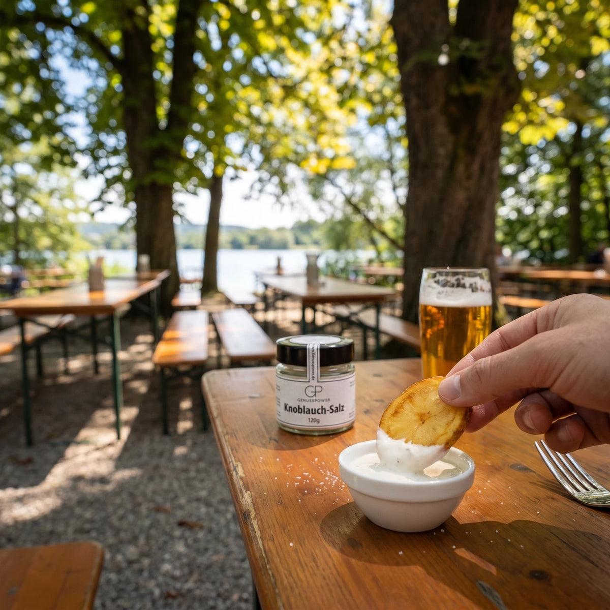 Eine Gabel tunkt eine Bratkartoffel in eine Schale Dip, daneben ein Glas Bier, das Salzglas weich im Hintergrund