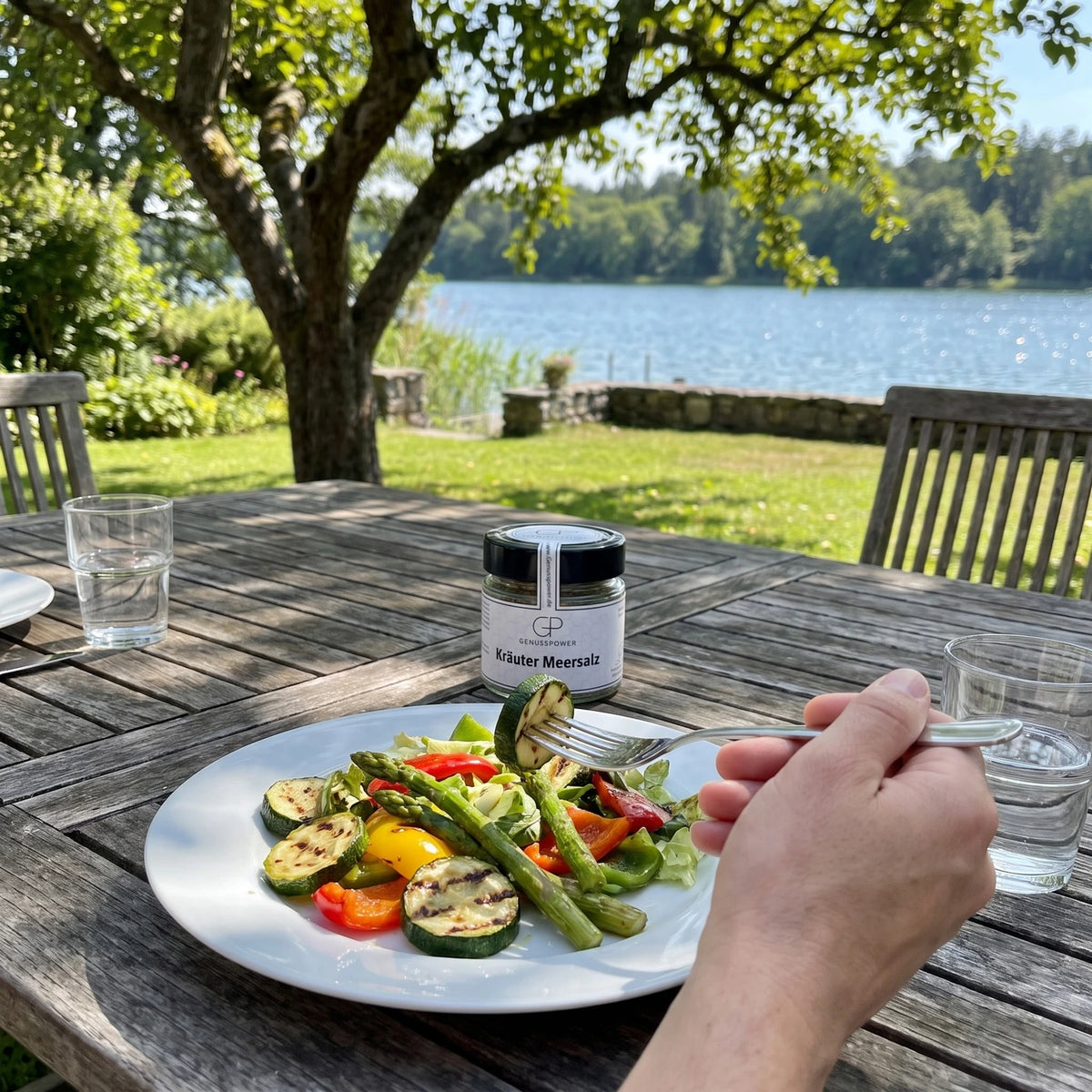 Teller mit Salat und gegrilltem Gemüse, eine Gabel mit Zucchini, das Glas weich im Hintergrund auf dem Gartentisch