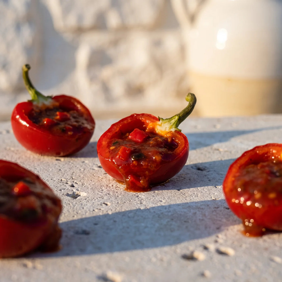 Halbierte Kirschpaprika, gefüllt mit der dunkelroten Sauce, auf hellem Stein