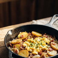 Eine schwarze Pfanne mit gebratenen Kartoffeln, Speck, Zwiebeln und gestocktem Ei, mit Schnittlauch bestreut