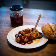 Currywurst in Scheiben auf einem Teller, mit dunkelroter Sauce und Currypulver bestäubt