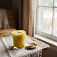 Ein Glas goldgelbe Golden Milk Latte mit Milchschaum und einer Prise Zimt