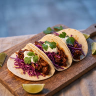 Drei Tacos mit zerfaserter, gebräunter Jackfruit, Rotkohl, Limette und Koriander auf einem Brett
