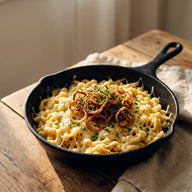 Eine gusseiserne Pfanne mit goldenen Käsespätzle, obendrauf knusprige Röstzwiebeln und Schnittlauch