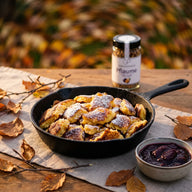 Kaiserschmarrn mit Puderzucker und dunklem Pflaumenkompott in einer Pfanne