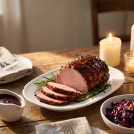 Ein glasierter Kasselerbraten in Scheiben auf einer Platte, daneben ein Kännchen dunkle Sauce und Rosmarinzweige