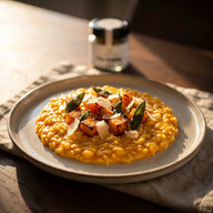 Oranges Kürbisrisotto auf einem flachen Teller mit gebratenen Kürbiswürfeln und Salbei