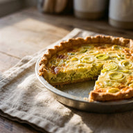 Eine goldgelbe Lauch-Quiche in einer runden Form, ein Stück herausgeschnitten
