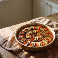 Eine runde Auflaufform mit Scheiben von Zucchini, Aubergine und Tomate, spiralförmig auf Tomatensauce geschichtet