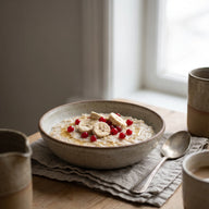 Eine Schale cremiger Porridge mit Bananenchips, roten Johannisbeeren und Honig