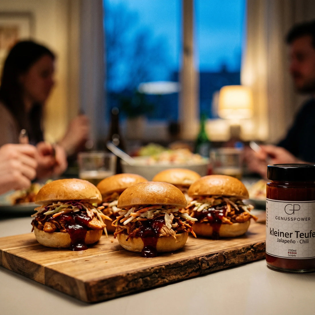 Kleine Brötchen gefüllt mit gezupftem Hähnchen in dunkler BBQ-Sauce und Krautsalat, daneben eine Flasche Kleiner Teufel