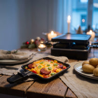 Ein Raclette-Pfännchen mit geschmolzenem Käse, Chorizoscheiben und bunten Paprikawürfeln