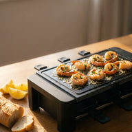 Gebratene rosa Garnelen in glänzender Knoblauchbutter mit Petersilie auf der heißen Grillplatte eines Raclette-Geräts