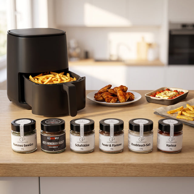 Airfryer Liebe: sechs Gewürzgläser vor einem offenen Airfryer mit Pommes, daneben Chicken Wings und Feta mit Tomaten auf einer hellen Küchenzeile