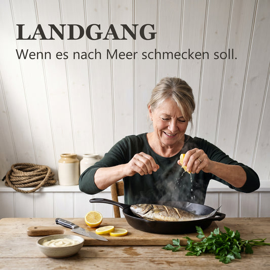 Landgang – Frau legt einen ganzen Fisch in die heiße Gusspfanne in einer Küche am Meer
