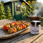 Gegrillte Hähnchenspieße mit Paprika auf einer Platte im Kleingarten am Abend, daneben African BBQ von Genusspower