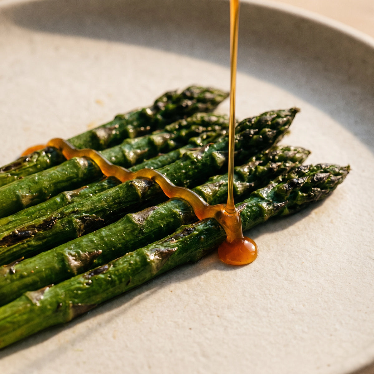 Goldener weißer Balsamico fällt in einem Faden auf gebratenen grünen Spargel und sammelt sich an einer Stange zu einem Tropfen