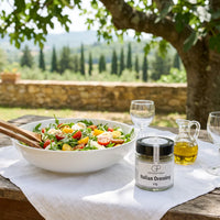Salat mit Rucola, Tomaten und Mozzarella in einer Keramikschüssel an einem Gartentisch in der Toskana, daneben Italian Dressing von Genusspower