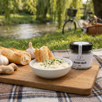 Aioli mit Baguette auf einem Holzbrett beim Picknick am Fluss, daneben Knobi-Aioli von Genusspower