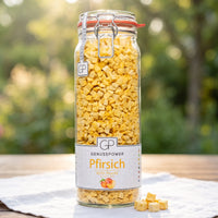 Großes Bügelglas gefriergetrocknete Pfirsich von Genusspower auf einem weißen Gartentisch im Morgenlicht
