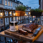 Gegrillte Spare Ribs auf einem Holzbrett auf einem Stadtbalkon am Abend, daneben Scharf auf Fleisch von Genusspower